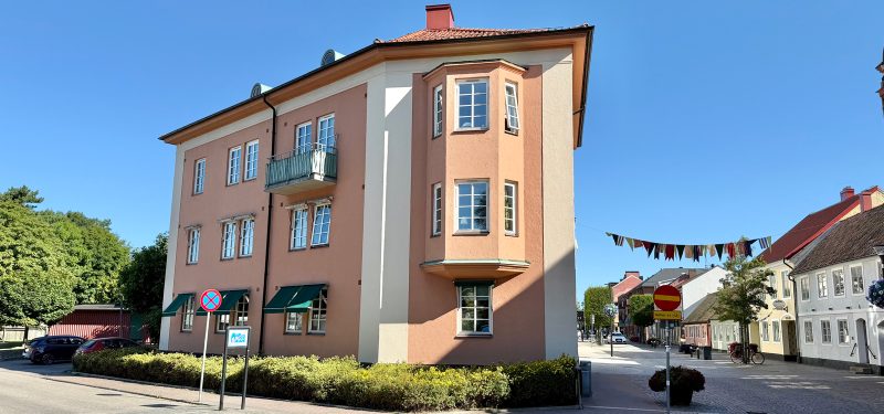 Storgatan 7, fasad mot korsningen Södra Kyrkogatan. Orangerosa putsfasad med krämvita detaljer och vita spröjsade fönster. Till höger skymtar Storgatan.