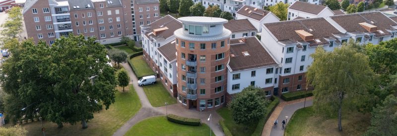 Flygvy från Nybrovägen där fastighetens runda torn i vinkeln och de två sidobyggnaderna visas. Tornet är i brunt tegel och sidodelarna i vit puts.