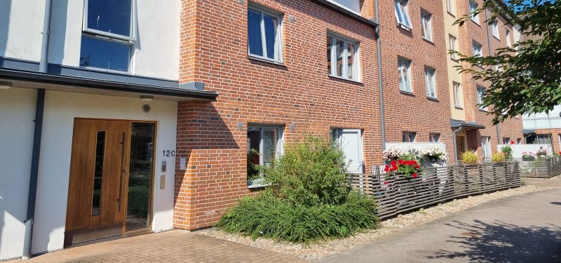 Entré till Sockerbruksgatan 12C, ekdörr med sidoljus. Trapphusets fasad beklädd med vit puts, övrig fasad i brunt tegel. Uteplatser mot innergården.