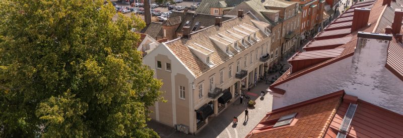 Stadsparkens grönskande träd syns i förgrunden i vänstra hörnet.Mitt i bild finns Storgatan 58s vita putsfasad mot Storgatan.