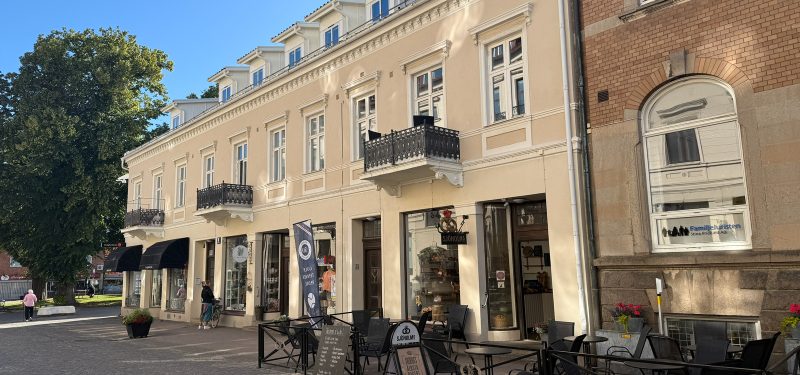 Storgatan 58, fasad mot Storgatan. Ljust rosagul putsfasad med vita knutar och foder. Butiker i bottenplan med stora fönsterpartier, två balkonger med smidesräcken mot gatan.