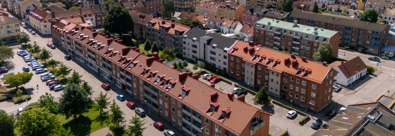 Flygvy över våra kvarter vid Nya Torg, Gasverksgaran 23-27 i förgrunden. Visar långa takåsar med tegelpannor, grönskande innergård och delar av Nya Torgs park i vänstra hörnet.