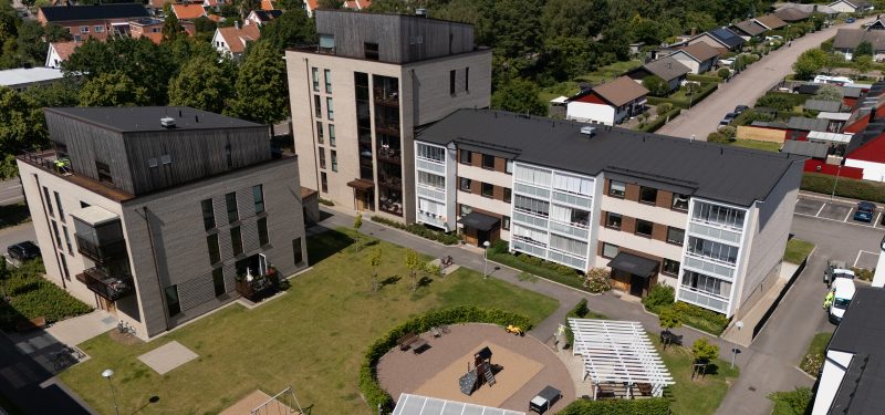 Flygvy över innergård med pergola och lekplats samt gräsyta och träd, i riktning mot 2A-B samt J-K.