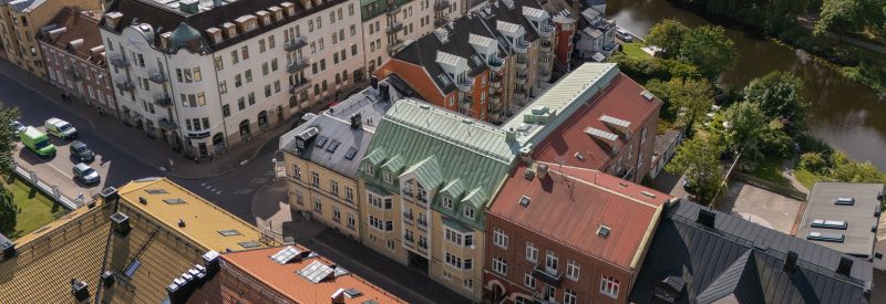 Flygvy över Västra Kyrkogatan 5-7 samt Järnvägsgatan 27 mot Järnvägsgatan. Gul putsad fasad och grönt plåttak. I bakgrunden skymtar ån.