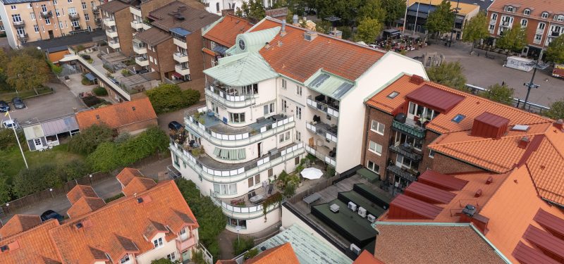 Flygvy över Järnvägsgatan 5-7:s baksida och terrasser- Vitputsad fastighet med bruna takpannor och detaljer i koppargrön plåt. Några indragna balkonger samt större terrasser.