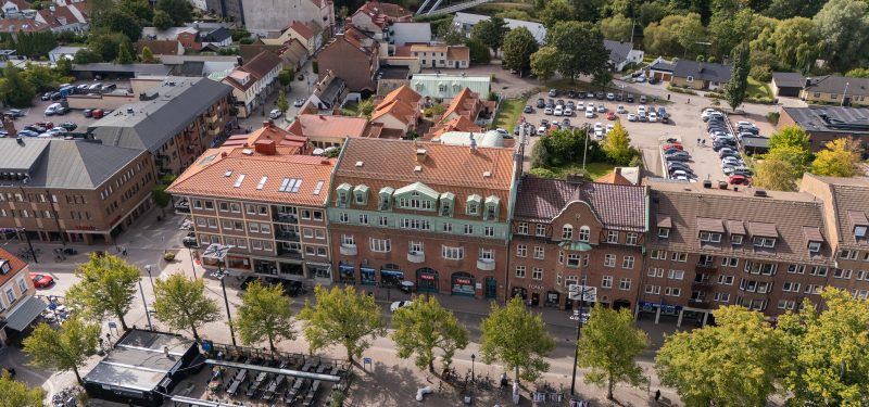 Flygvy över kvarteren Vakteln med torget i förgrunden. I mitten ligger Järnvägsgatan 6, ett brunt tegelhus med tegeltak, franska balkonger på översta våningen ut mot stortorget.