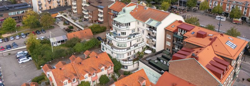 Flygvy över Järnvägsgatan 5-7:s baksida och terrasser- Vitputsad fastighet med bruna takpannor och detaljer i koppargrön plåt. Några indragna balkonger samt större terrasser.