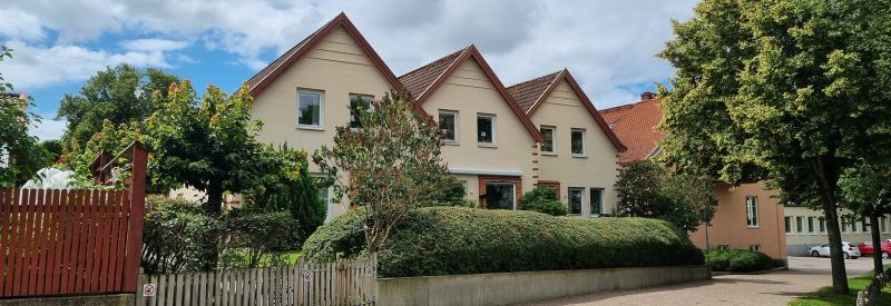 Tre radhus i vit putsad fasad med vita fönster. Buskar och träd i förgrunden.