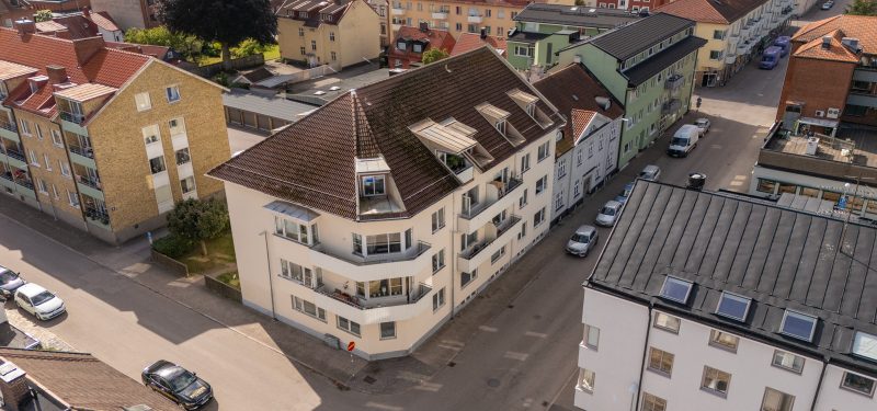 Flygvy över Sandvångsgatan 9A-B sett från nordöst. Visar fastighet på tre plan plus vindsvåning med gräddvit putsfasad och brunt tak. Balkonger med vit plåtfron som vetter ut mot gatan (nordöst).