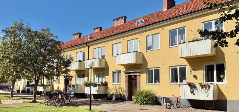Flerbostadshus i två våningar plus vind, med gul putsfasad, vita sidohängda fönster och brunt tegeltak. Balkonger med vita plåtfronter. Fasaden vetter mot kvarterets innergård med gräsmatta och träd.