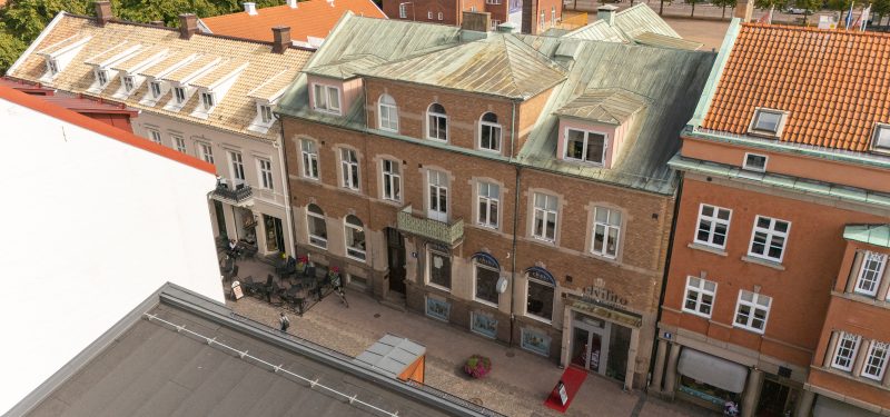 Storgatan 56, fasad mot Storgatans gångstråk. Hus i två våningar, med lokaler i bottenplan. Fasad klädd i ljusbrun tegel, vita flaggfönster och koppargrönt tak.