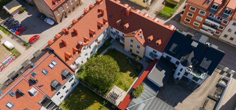 Flygvy över Gasverksgatan 19/Vaktgatan 16 och dess innergård med gräsyta, uteplats under pergola och stort träd.