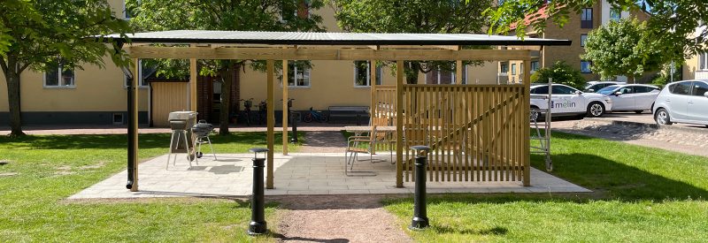 Gräsyta som delas av en grusgång till en plattlagd yta där en pergola har byggts.