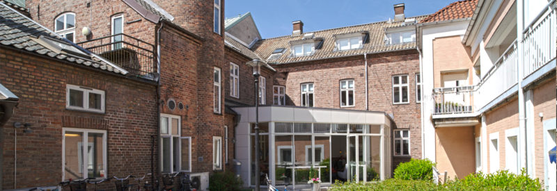 Innergård omgiven av tegelbyggnader med fönster, balkonger och en modernt uterum för ett café.