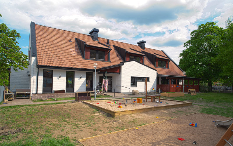 Ett tvåvåningshus med rött tak, vita väggar och en sandlåda samt gräsyta i förgrunden.