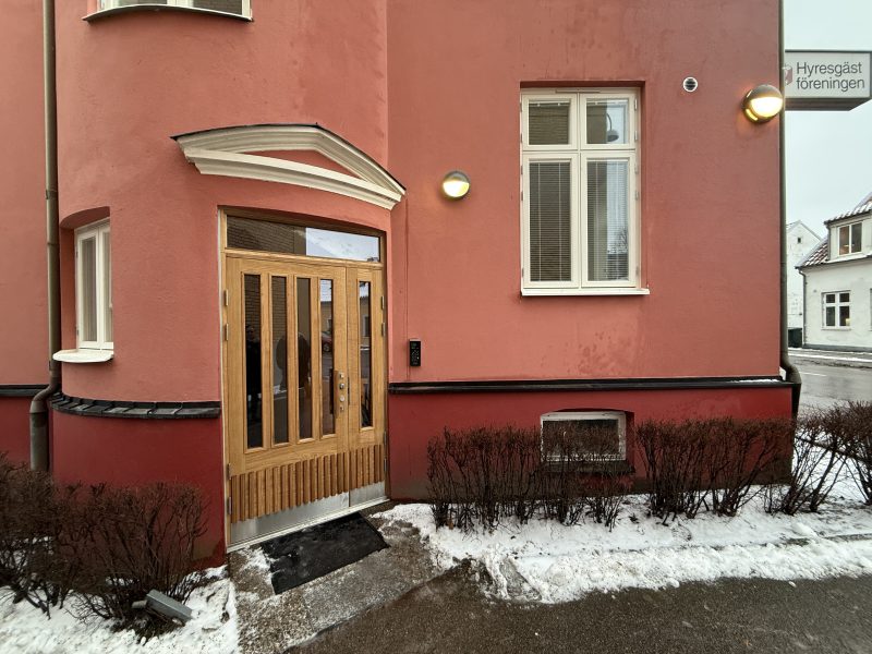 Fastighet med ljusröd putsfasad, ny entrédörr i ek samt nya vita flaggfönster i trä.