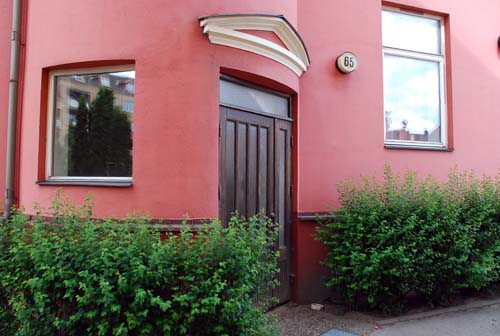 Fastighet med ljusröd putsfasad, äldre entrédörr i ek samt vita fönster.