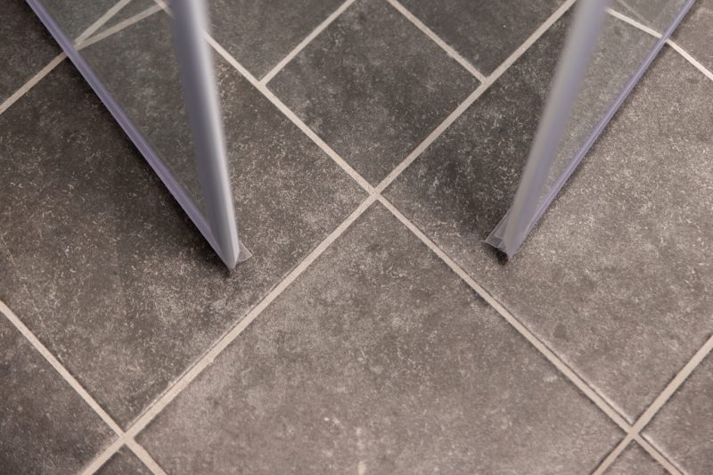 Närbild på grå klinjker med ljusa fogar och en del av duschväggar.